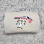 Make Goose Great Again sweatshirt in Sand with an embroidered white goose waving an American flag under red and blue letters