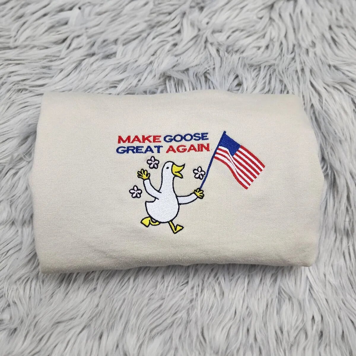Make Goose Great Again Sweatshirt – Sand Make Goose Great Again sweatshirt in Sand with an embroidered white goose waving an American flag under red and blue letters