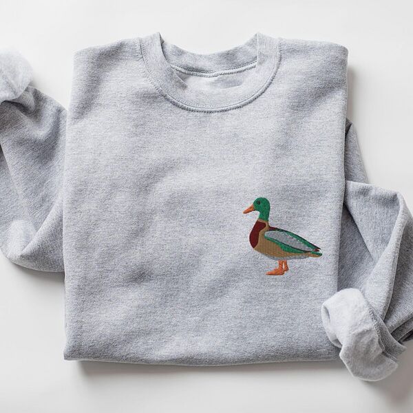 Sport Grey crewneck sweatshirt laid flat with a rolled cuff, embroidered with a standing drake mallard with a green head, orange bill, chestnut chest and grey wing on the left chest