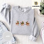 Ash crewneck sweatshirt folded with denim shorts, white sneakers and a potted plant, embroidered with three mallard ducks in Santa hats, knit scarves and orange boots carrying a string of Christmas lights