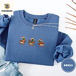 Indigo Blue crewneck sweatshirt folded with light jeans and dried twigs, embroidered with three mallard ducks in Santa hats, knit scarves and orange boots carrying a string of Christmas lights