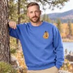 Man wearing the Heather Deep Royal Pomeranian Halloween sweatshirt by a pine tree on a fall day