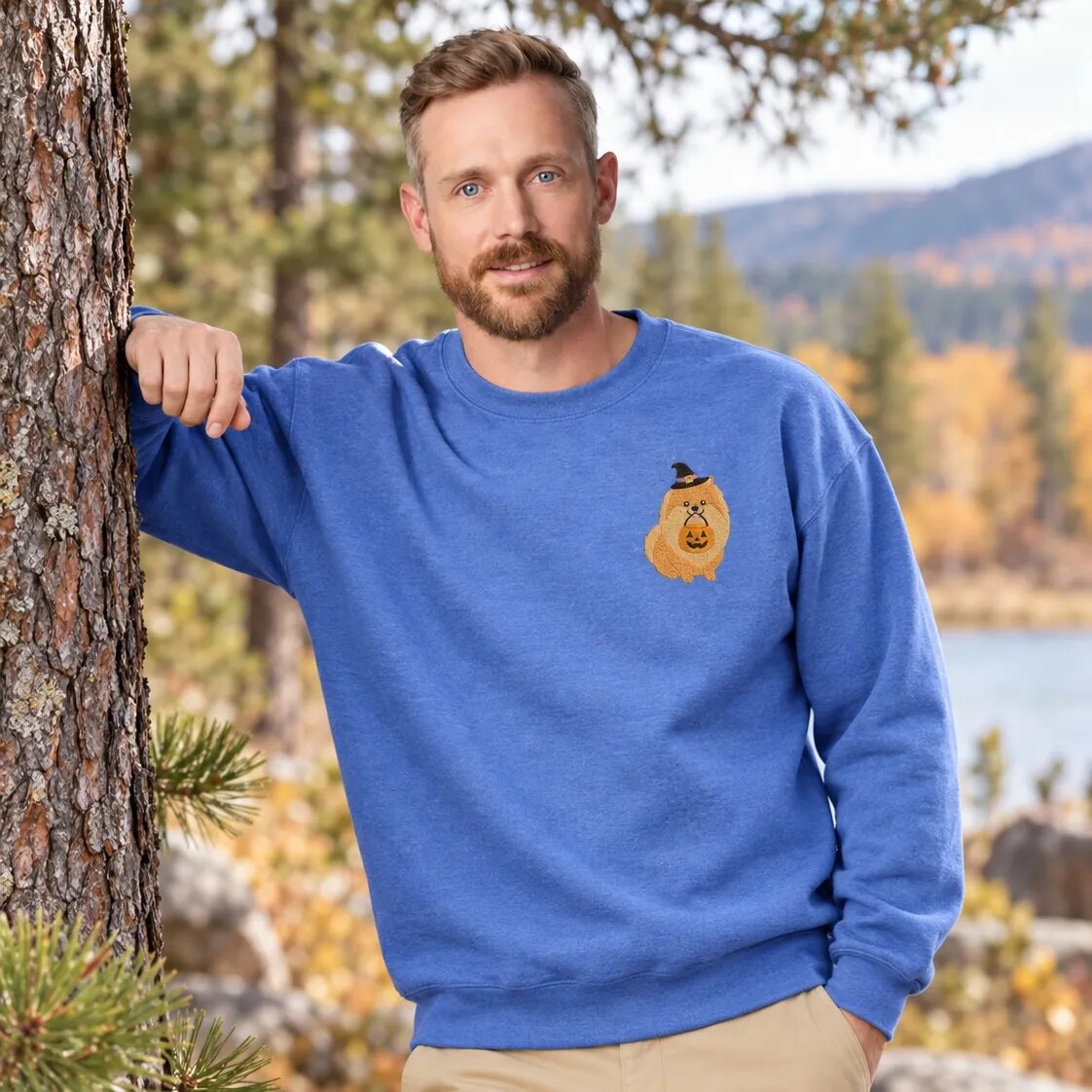 Man Wearing the Pomeranian Halloween Sweatshirt Man wearing the Heather Deep Royal Pomeranian Halloween sweatshirt by a pine tree on a fall day