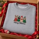 Meowy Christmas sweatshirt folded in a gift box with red tissue paper and a cat toy