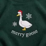 Close-up of the embroidered merry goose design: a white goose in a red Santa hat between two snowflakes