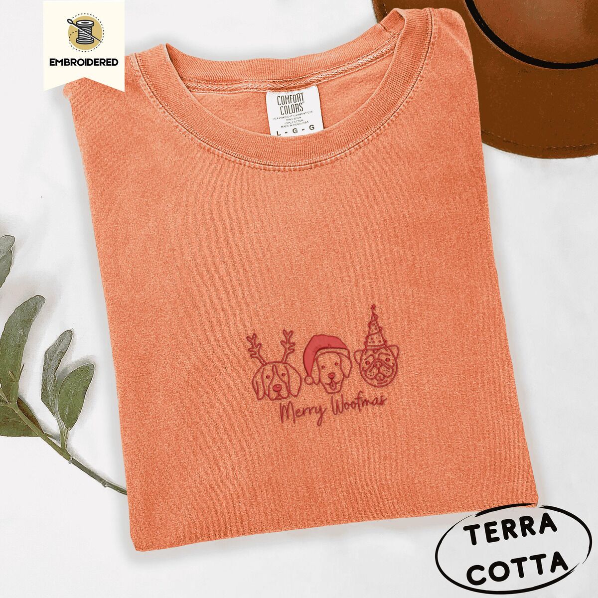 Merry Woofmas Shirt – Terracotta Terracotta Comfort Colors T-shirt embroidered with three red line-art dog faces in Christmas hats above Merry Woofmas script
