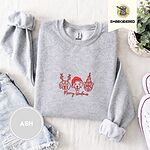 Ash crewneck sweatshirt folded with denim shorts, white sneakers and a potted plant, embroidered with three red line-art dog faces, a beagle in reindeer antlers, a retriever in a Santa hat and a pug in a party hat, above Merry Woofmas in script