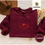 Maroon crewneck sweatshirt with a brown felt hat and dried bunny tail grass, embroidered with three red line-art dog faces, a beagle in reindeer antlers, a retriever in a Santa hat and a pug in a party hat, above Merry Woofmas in script