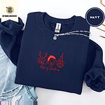 Navy crewneck sweatshirt folded with ripped jeans and a silver chain necklace, embroidered with three red line-art dog faces, a beagle in reindeer antlers, a retriever in a Santa hat and a pug in a party hat, above Merry Woofmas in script