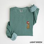 Mini goldendoodle Christmas sweatshirt in Light Green laid flat with rolled cuffs, embroidered with a small doodle in a red Santa hat on the left chest