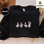 Black crewneck sweatshirt with a brown felt hat and dried bunny tail grass, embroidered with four white ducks holding a clipboard, a syringe, a stethoscope and a bandage