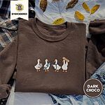 Dark Chocolate crewneck sweatshirt on a plaid flannel shirt with yellow autumn leaves and denim shorts, embroidered with four white ducks holding a clipboard, a syringe, a stethoscope and a bandage