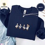 Navy crewneck sweatshirt folded with ripped jeans and a silver chain necklace, embroidered with four white ducks holding a clipboard, a syringe, a stethoscope and a bandage