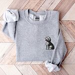 Sport Grey crewneck sweatshirt laid flat on a herringbone wood floor, embroidered with a shaggy Old English sheepdog sitting in profile with a white front, a dark back and a red tongue on the left chest