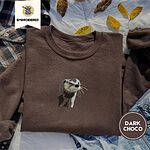 Dark Chocolate crewneck sweatshirt on a plaid flannel shirt with yellow autumn leaves and denim shorts, embroidered with a river otter head in brown and cream thread with long golden whiskers