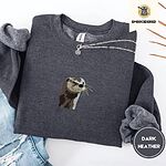 Dark Heather crewneck sweatshirt folded with ripped jeans and a silver chain necklace, embroidered with a river otter head in brown and cream thread with long golden whiskers