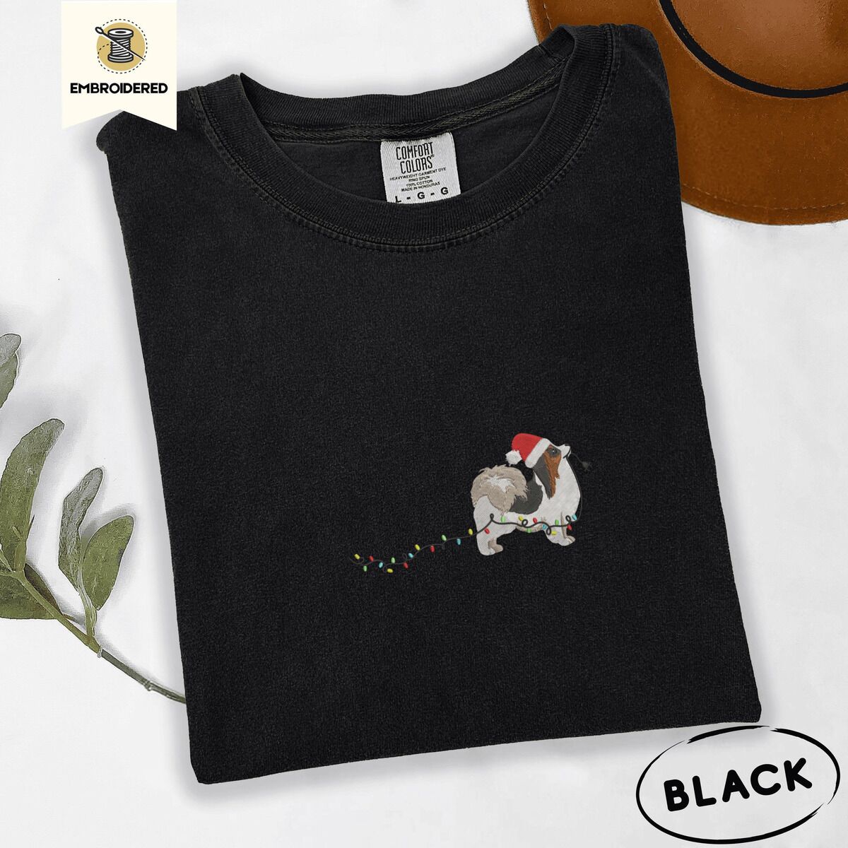 Papillon Christmas Lights Shirt – Black Black Comfort Colors T-shirt embroidered with a tricolor Papillon in a Santa hat holding the plug of a string of Christmas lights in its mouth