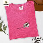 Crunchberry Comfort Colors T-shirt embroidered with a tricolor Papillon in a Santa hat holding the plug of a string of Christmas lights in its mouth