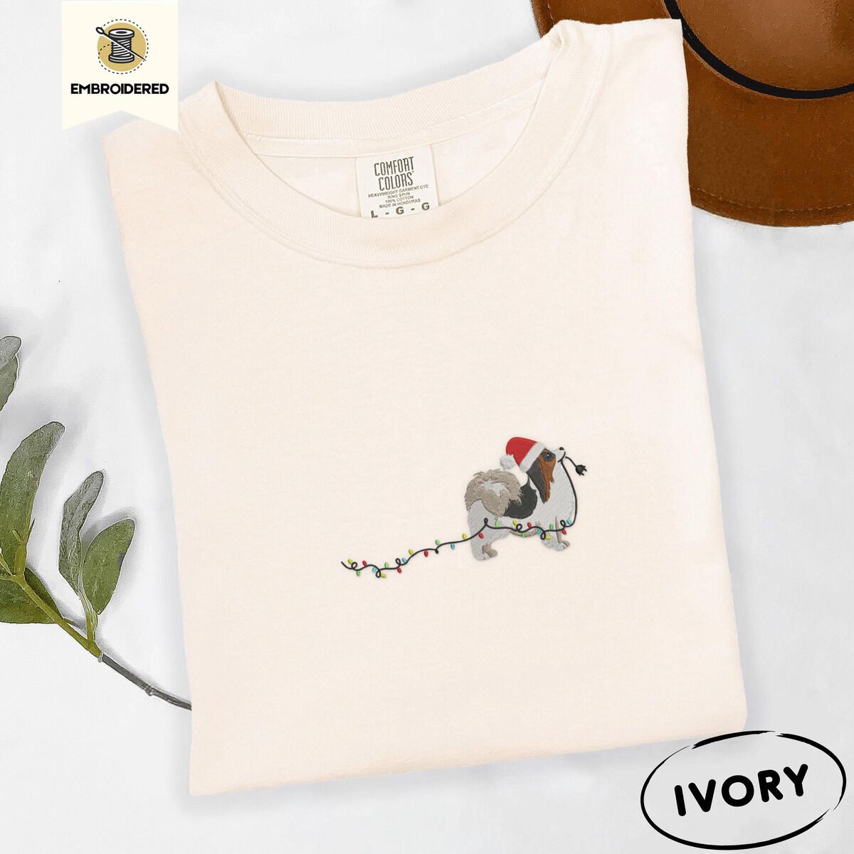 Papillon Christmas Lights Shirt – Ivory Ivory Comfort Colors T-shirt embroidered with a tricolor Papillon in a Santa hat holding the plug of a string of Christmas lights in its mouth
