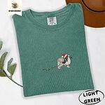 Light Green Comfort Colors T-shirt embroidered with a tricolor Papillon in a Santa hat holding the plug of a string of Christmas lights in its mouth
