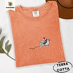 Terracotta Comfort Colors T-shirt embroidered with a tricolor Papillon in a Santa hat holding the plug of a string of Christmas lights in its mouth