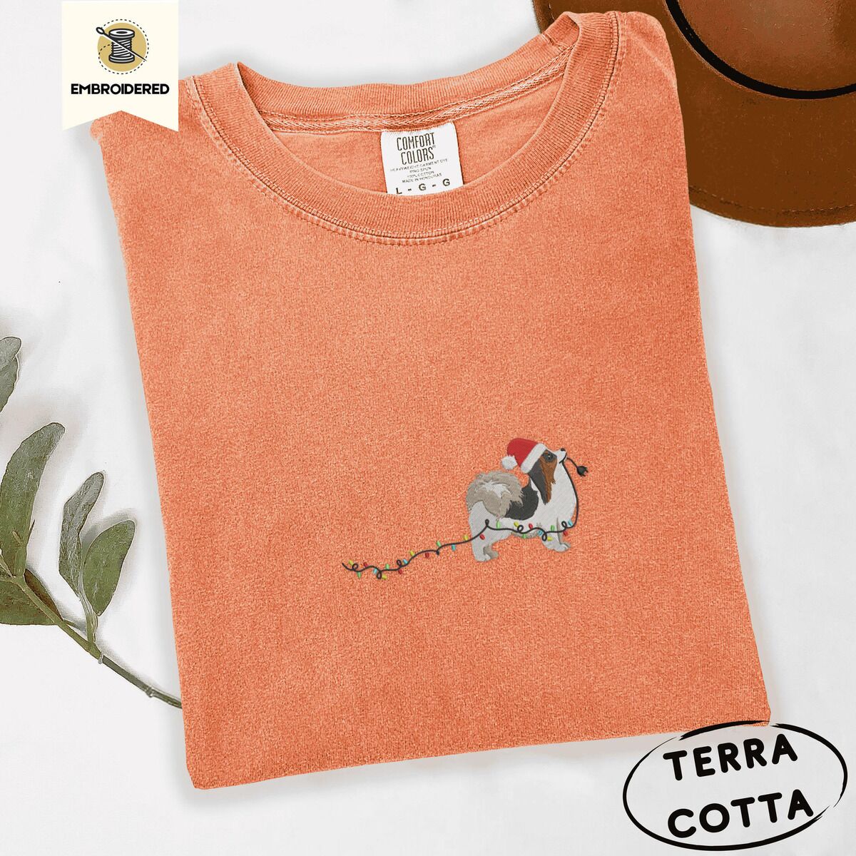 Papillon Christmas Lights Shirt – Terracotta Terracotta Comfort Colors T-shirt embroidered with a tricolor Papillon in a Santa hat holding the plug of a string of Christmas lights in its mouth