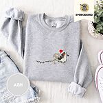 Ash crewneck sweatshirt folded with denim shorts, white sneakers and a potted plant, embroidered with a tricolor Papillon in a Santa hat holding the plug of a string of Christmas lights in its mouth