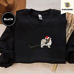 Black crewneck sweatshirt with a brown felt hat and dried bunny tail grass, embroidered with a tricolor Papillon in a Santa hat holding the plug of a string of Christmas lights in its mouth