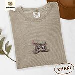 Khaki Comfort Colors T-shirt embroidered with a fluffy brown tabby kitten peeking over a ledge at a pink butterfly