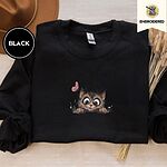 Black crewneck sweatshirt with a brown felt hat and dried bunny tail grass, embroidered with a fluffy brown tabby kitten with big round eyes peeking over a ledge at a pink butterfly