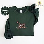 Forest Green crewneck sweatshirt folded on a white background, embroidered with a fluffy brown tabby kitten with big round eyes peeking over a ledge at a pink butterfly