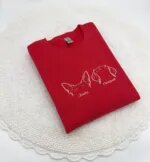 Folded red personalized dog ears sweatshirt on a white crochet mat