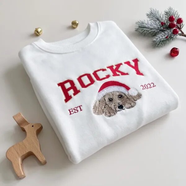 Personalized dog name Christmas sweatshirt with ROCKY in red varsity letters, an embroidered dog portrait in a Santa hat and EST 2022