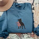 Indigo Blue crewneck sweatshirt beside a hat and dried grass, a black pit bull with an American flag stitched across the chest