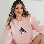 Smiling woman in a Light Pink crewneck sweatshirt embroidered with a pit bull silhouette and a small flag