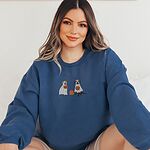 Smiling woman sitting in a blue crewneck sweatshirt, embroidered with a pit bull and a black lab in ghost sheets holding jack-o'-lantern buckets