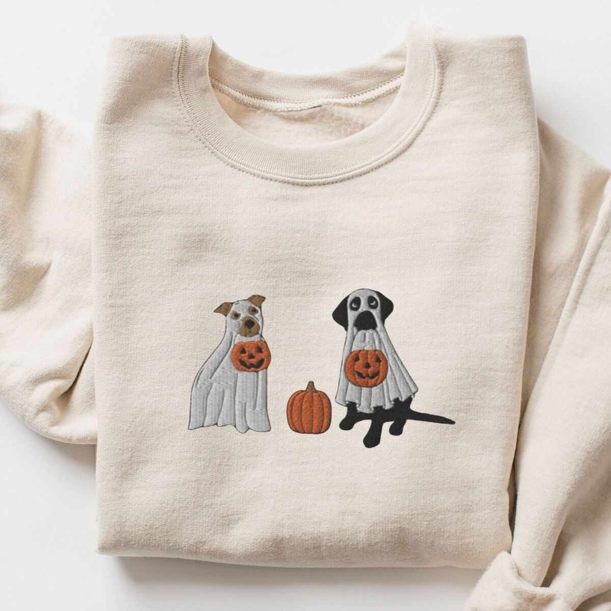 Pitbull and Black Lab Sweatshirt – Sand Sand crewneck sweatshirt laid flat with a rolled cuff, embroidered with a pit bull and a black lab in ghost sheets holding jack-o'-lantern buckets