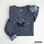 Denim crewneck sweatshirt laid flat with a rolled cuff, embroidered with a black pitbull silhouette in a play bow with a red scarf, holding a string of Christmas lights under white snowflakes