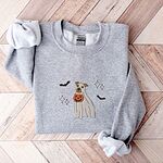 Sport Grey crewneck sweatshirt laid flat on a chevron wood floor, embroidered with a pit bull in a ghost sheet holding a jack-o'-lantern bucket between bats and sparkles