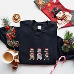 Black crewneck sweatshirt laid flat with a Christmas stocking, candy cane and coffee, embroidered with three sitting pitbulls, fawn, white and black, in red Santa hats and red scarves