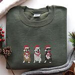 Military Green crewneck sweatshirt laid flat with pinecones and a knit blanket, embroidered with three sitting pitbulls, fawn, white and black, in red Santa hats and red scarves
