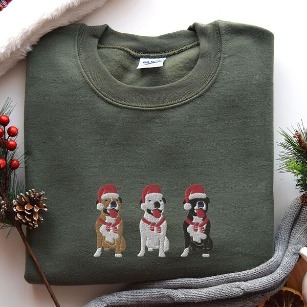 Military Green crewneck sweatshirt laid flat with pinecones and a knit blanket, embroidered with three sitting pitbulls, fawn, white and black, in red Santa hats and red scarves