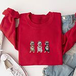 Red crewneck sweatshirt laid flat with jeans and white sneakers, embroidered with three sitting pitbulls, fawn, white and black, in red Santa hats and red scarves