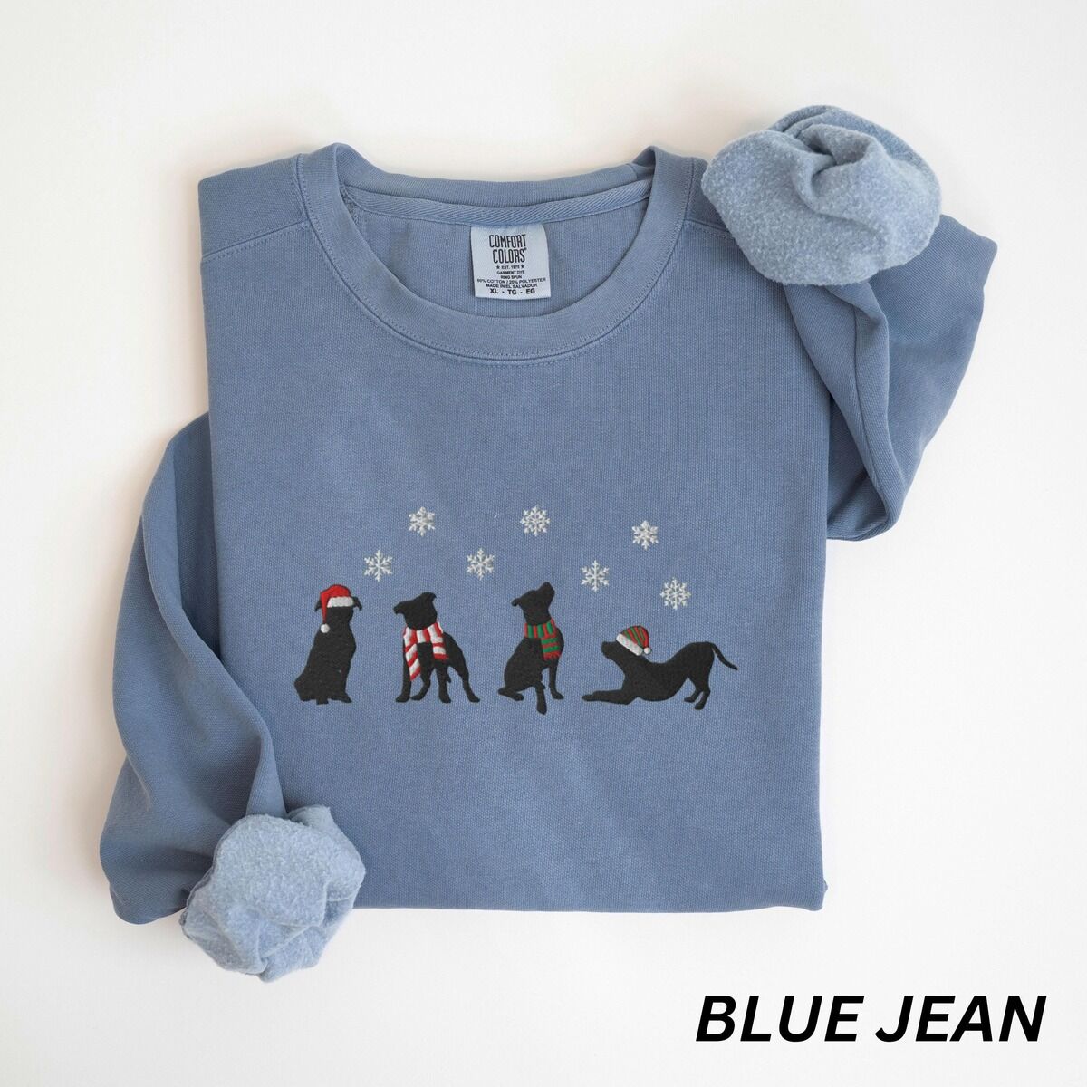 Pitbull Silhouette Christmas Sweatshirt – Blue Jean Blue Jean crewneck sweatshirt laid flat with a rolled cuff, embroidered with four black pitbull silhouettes in a Santa hat, striped scarves and a knit hat under snowflakes