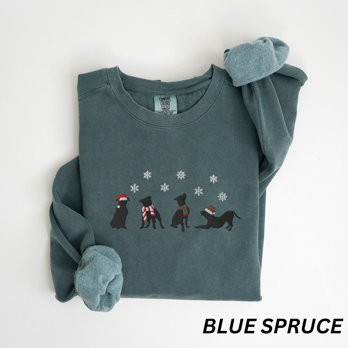 Pitbull Silhouette Christmas Sweatshirt – Blue Spruce Blue Spruce crewneck sweatshirt laid flat with a rolled cuff, embroidered with four black pitbull silhouettes in a Santa hat, striped scarves and a knit hat under snowflakes