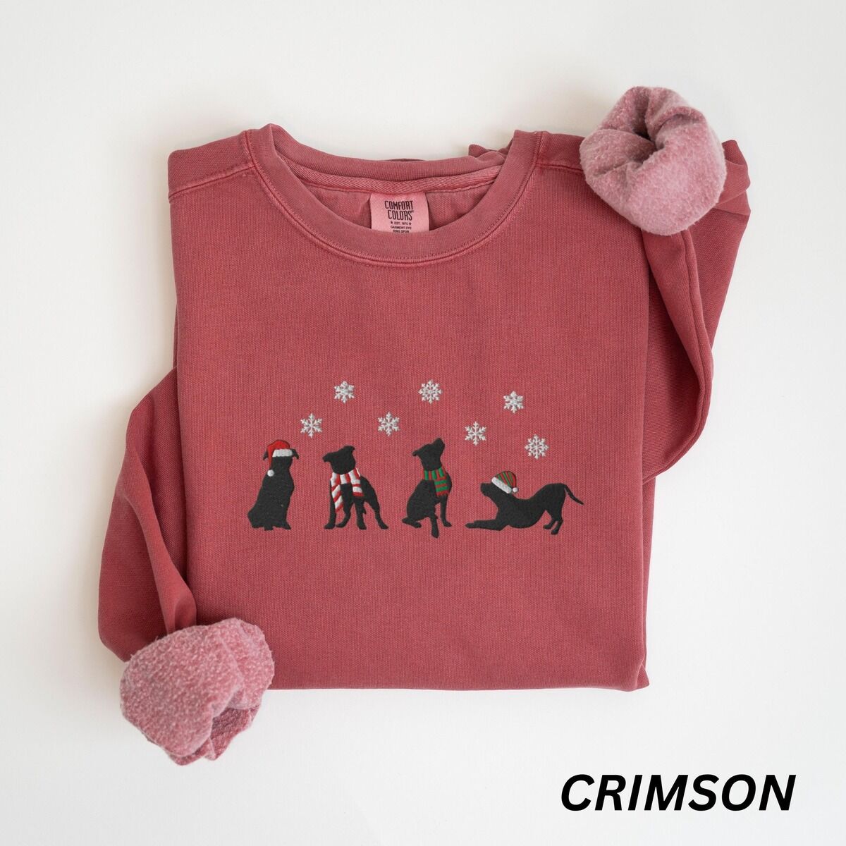 Pitbull Silhouette Christmas Sweatshirt – Crimson Crimson crewneck sweatshirt laid flat with a rolled cuff, embroidered with four black pitbull silhouettes in a Santa hat, striped scarves and a knit hat under snowflakes