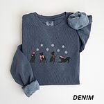 Denim crewneck sweatshirt laid flat with a rolled cuff, embroidered with four black pitbull silhouettes in a Santa hat, striped scarves and a knit hat under snowflakes