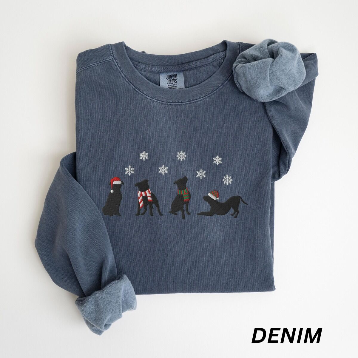 Pitbull Silhouette Christmas Sweatshirt – Denim Denim crewneck sweatshirt laid flat with a rolled cuff, embroidered with four black pitbull silhouettes in a Santa hat, striped scarves and a knit hat under snowflakes