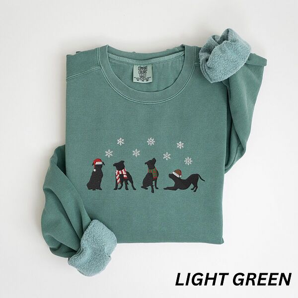 Light Green crewneck sweatshirt laid flat with a rolled cuff, embroidered with four black pitbull silhouettes in a Santa hat, striped scarves and a knit hat under snowflakes