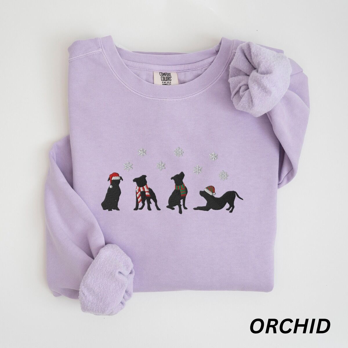 Pitbull Silhouette Christmas Sweatshirt – Orchid Orchid crewneck sweatshirt laid flat with a rolled cuff, embroidered with four black pitbull silhouettes in a Santa hat, striped scarves and a knit hat under snowflakes